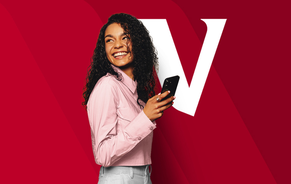 A woman is pink shirt standing and looking behind her while holding her phone in front of her