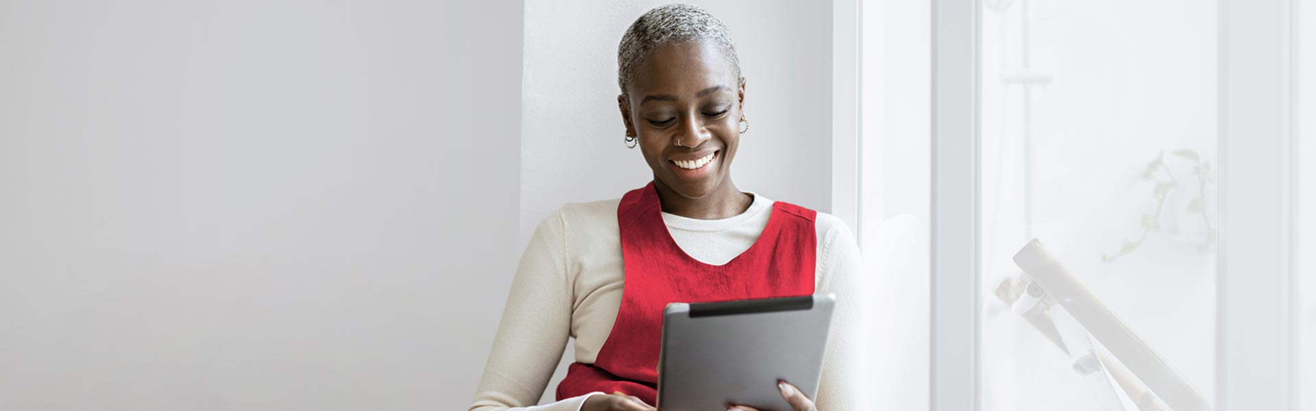 Person using their tablet computer while standing by a window and smiling.
