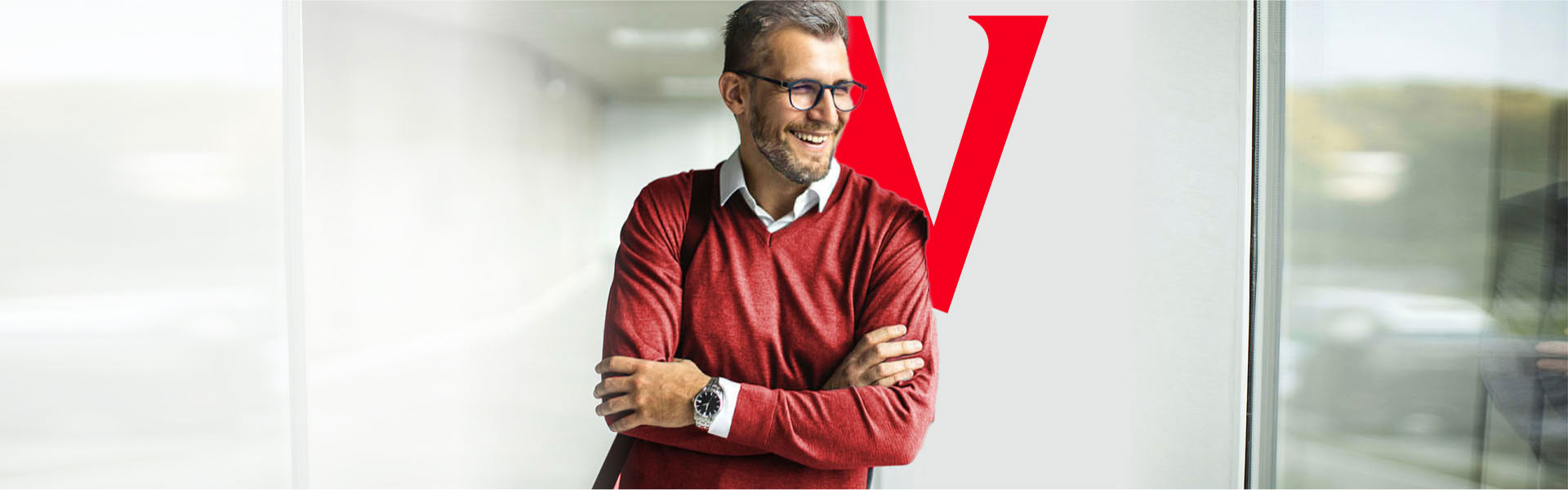 A middle-aged man stands with his arms crossed and is smiling and laughing.