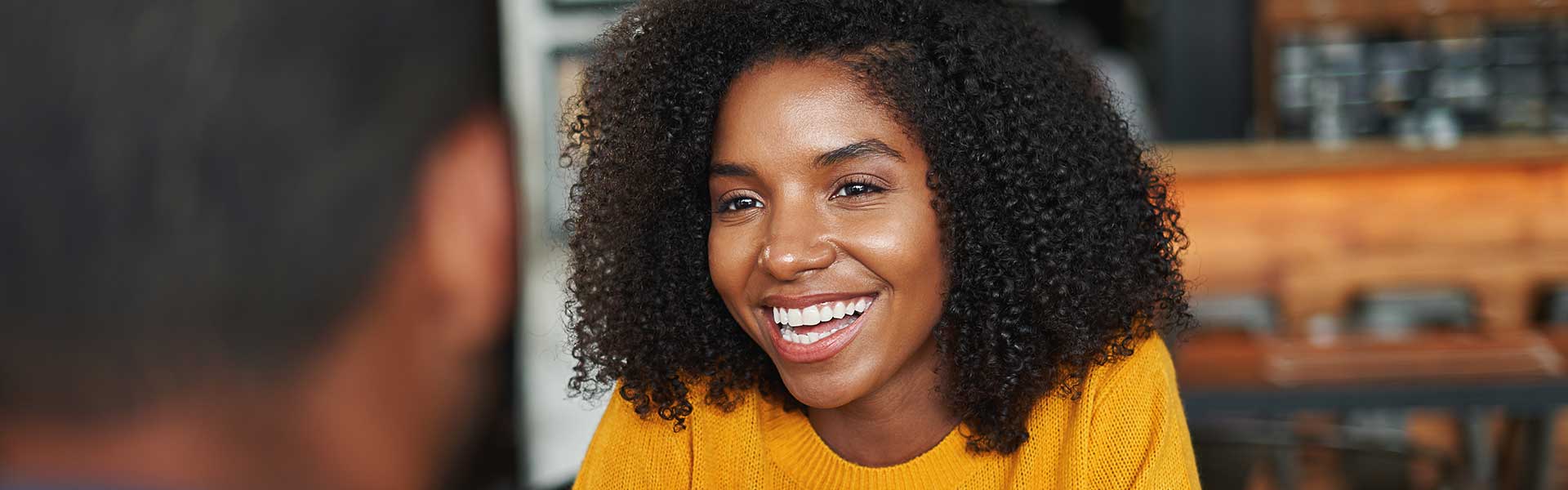 A woman smiles during a conversation with a friend in a coffee shop.