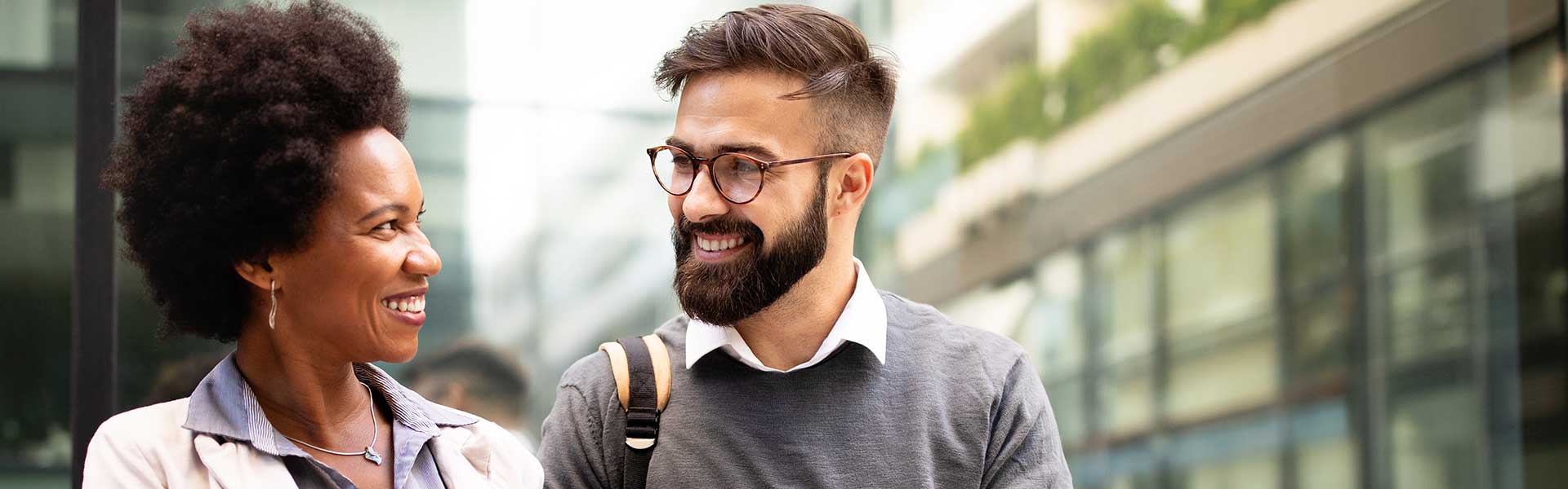 Two coworkers standing in front of their office smile as they have a conversation
