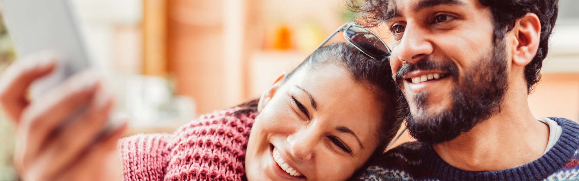 A young, smiling couple is looking at a shared phone screen.