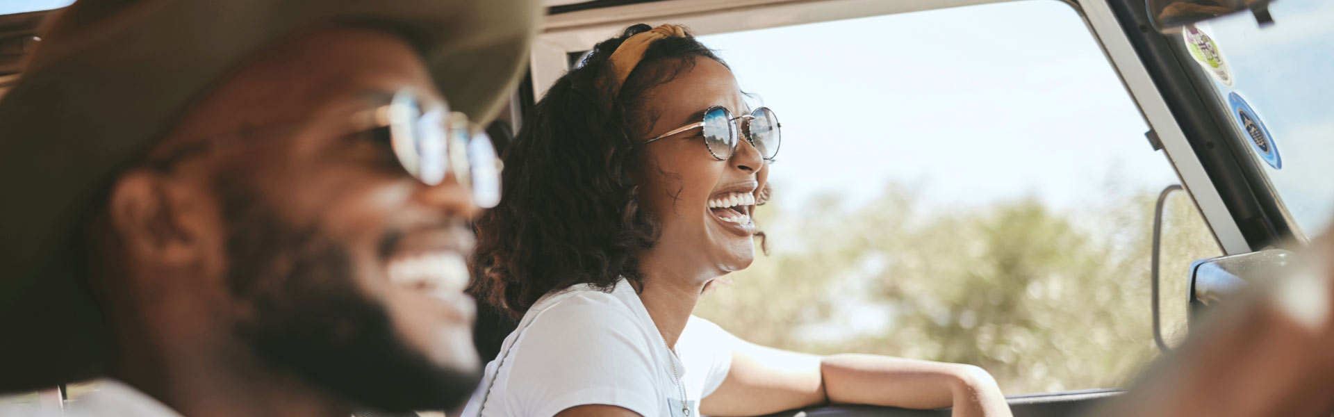 Man and woman enjoying a car ride and sharing a laugh on a sunny day.