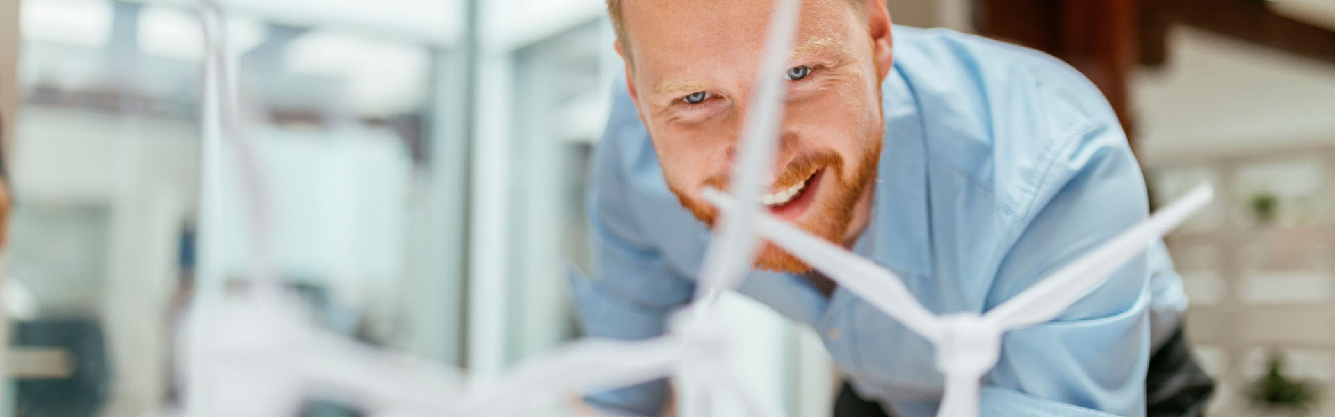 A man is bending down to look at small model wind turbines.	