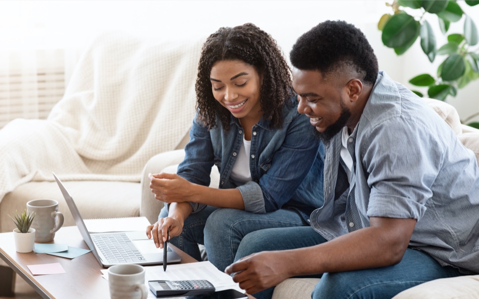 Smiling couple on sofa, looking at a laptop.