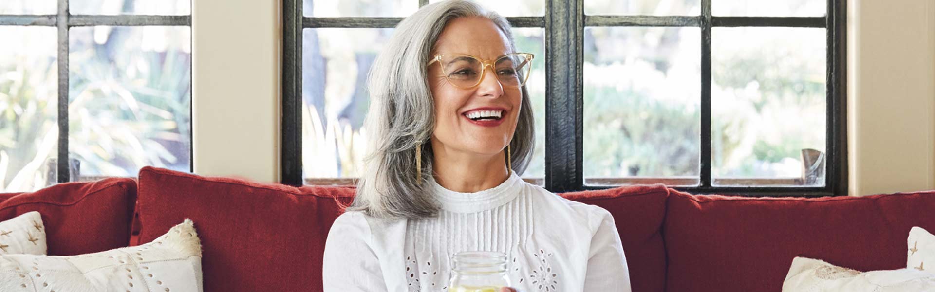 Woman wearing glasses sitting on a red couch and smiling.